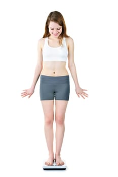 Happy fit young woman standing on bathroom scale looking down