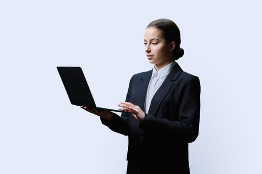 Serious teenage female student in black jacket using laptop on white studio background. Education, learning, technology, knowledge concept