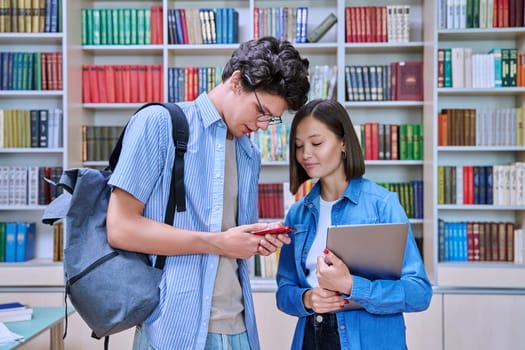 Cheerful talking college students male and female with books backpacks meeting inside library. Friendship, communication, knowledge, education, university college youth concept