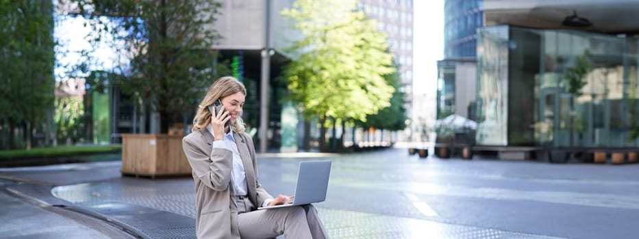 Businesswoman checking diagram and work on laptop, calling someone on mobile phone, sitting outdoors in city centre.