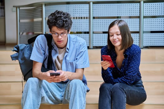 Friends classmates college students guy and girl with smartphones inside educational building. Youth, lifestyle, technology, mobile applications for learning leisure communication