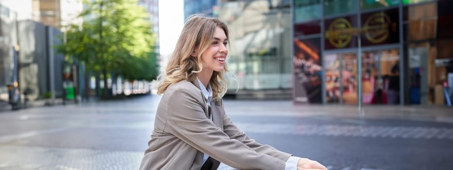 Businesswoman smiles as sits in city center, wears beige suit for office work.