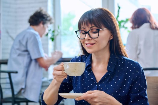 Relaxed happy middle aged woman enjoying fragrant fresh tasty cup of coffee while sitting in coffee shop. Coffee culture, lifestyle, people concept