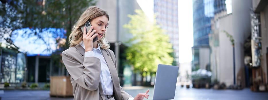 Businesswoman checking diagram and work on laptop, calling someone on mobile phone, sitting outdoors in city centre.