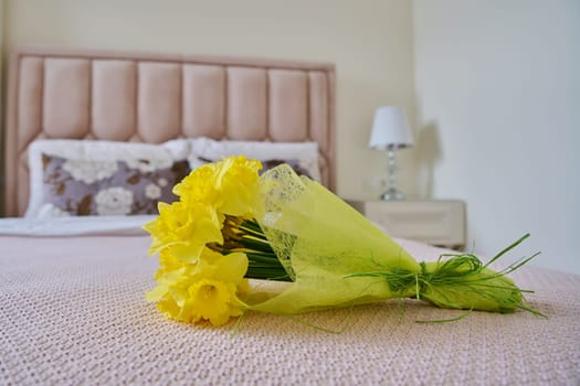 Bouquet of yellow flowers on bed in bedroom, classic interior in pink pastel colors