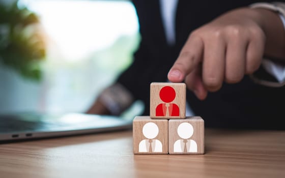 Wooden blocks with printed manager icons selected by businessmen to express human resource management and leadership concepts.