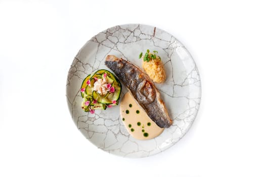 Sea bass or dorado fillet with baked zucchini and sauce on a gray plate isolated