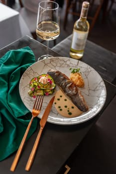Sea bass or dorado fillet with baked zucchini and sauce on a gray plate in a restaurant