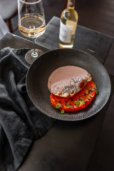 Sea bass or dorado fillet with sweet potato puree and flying fish roe sauce on a black plate in a restaurant