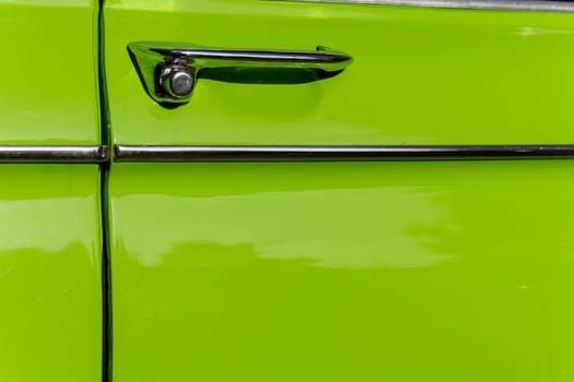 metal chrome door opening handle of an old classic car of light green color. Details of retro cars. close-up and attention to detail. The door lock is built into the handle.