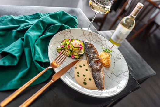 Sea bass or dorado fillet with baked zucchini and sauce on a gray plate in a restaurant