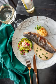 Sea bass or dorado fillet with baked zucchini and sauce on a gray plate in a restaurant