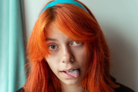 funny teen girl with red hair shows blue tongue. The girl is fooling around.