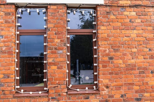 large windows in a red brick wall. Industrial design in the design of a city cafe or restaurant. Garlands of light bulbs around the windows.