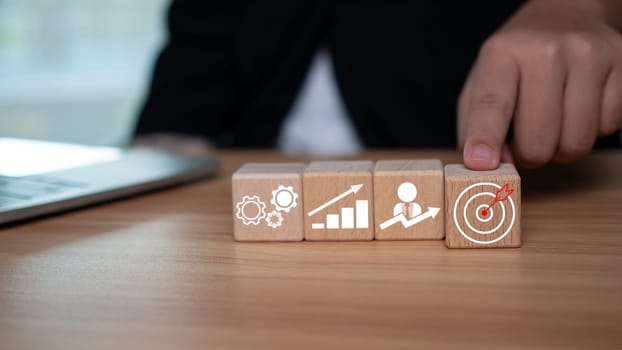 A businessman points to a dart board printed on square wooden blocks representing setting business goals.