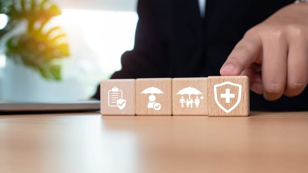 Businessman points his finger at a wooden block printed with insurance icons representing the concept of health insurance and medical benefits and healthcare planning.