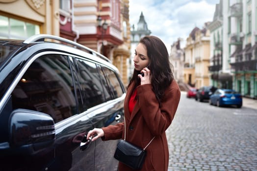 A Successful young woman with long hair in a red coat talks on the phone and gets into her car