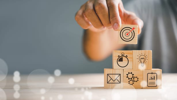 Businessman's hand stacking wood blocks with an icon, depicting the importance of business strategy and Action plan. Copy space available for professional projects.