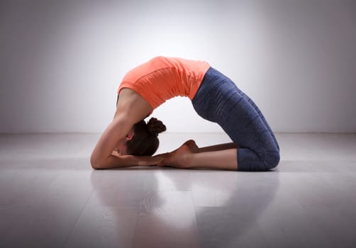 Beautiful sporty fit yogini woman practices yoga asana Kapotasana - pigeon pose intense backbend in studio