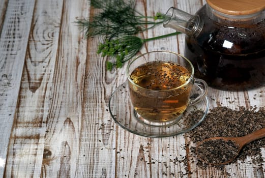 Medicinal tea using dried dill seeds in a cup and teapot on a natural wooden table.