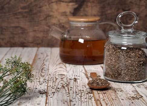 The concept of the usefulness of dill. Medicinal tea using dried dill seeds in a cup and teapot on a natural wooden table