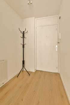 an empty room with wood floors and white walls, including a black coat rack on the door to the left