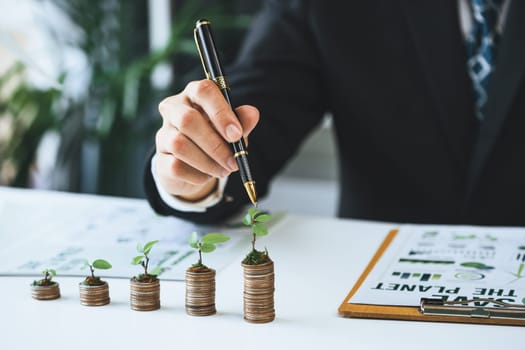 Businessman with coin stack at his office as sustainable money growth investment or eco-subsidize. Green corporate promot and invest in environmental awareness. Gyre