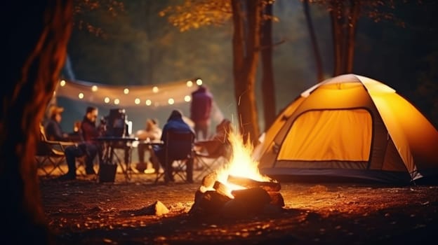 Picnic fire in the foreground is in focus. Blurred background with people and the yellow tent. AI