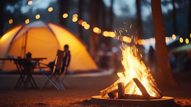 Picnic fire in the foreground is in focus. Blurred background with people and the yellow tent. AI