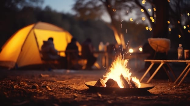 Picnic fire in the foreground is in focus. Blurred background with people and the yellow tent. AI