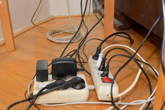 Tangled cables in the extension cord. Messy cables. Cables tangled on parquet flooring