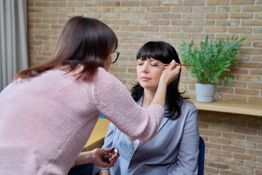 Makeup artist doing makeup for a mature business woman. Beauty, cosmetics, care, face, 50 years old woman