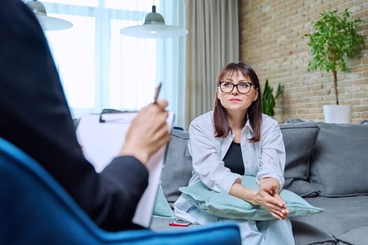 Middle-aged woman at meeting with psychologist counselor, sitting on couch in office. Mental problems of age female, psychological support help. Psychology psychotherapy therapy treatment healthcare