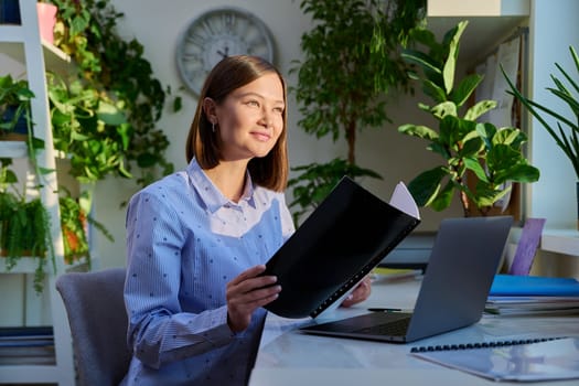 Portrait of young woman sitting at home at desk with computer laptop, smiling positive female university student, freelancer, remote worker. Study work technology lifestyle 20s youth