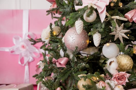 Giftboxes, pink and white christmas decorations balls hanging on a decorative white christmas tree.