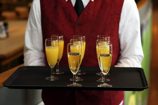 Waiter serves sparkling wine and orange juice on a tray
