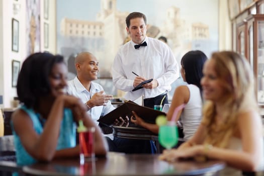 young adult hispanic couple dining out in restaurant and talking to waiter in bow tie. Horizontal shape, front view, waist up