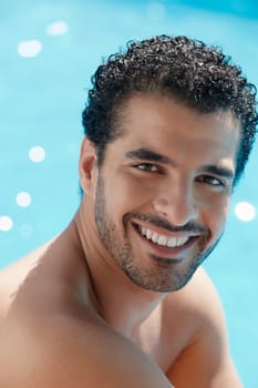 Handsome happy young hispanic man smiling and relaxing near hotel pool. Vertical shape, head and shoulders