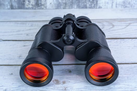 Close-up of black binoculars with red-tinted lenses placed on a white wooden surface, symbolizing exploration, vision, and outdoor adventure.