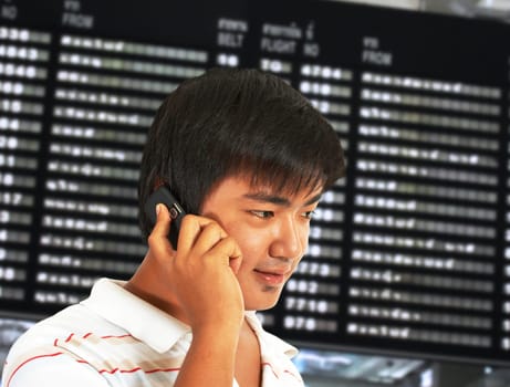 Man talking on his mobile phone in front of a departure board in an airport