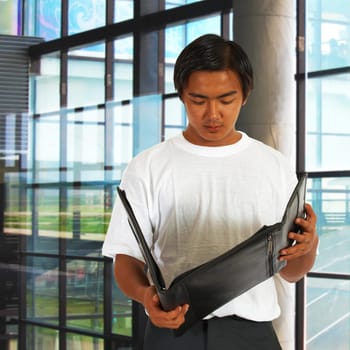 Office Worker Standing By The Window And Checking Notes In A Leather Folder