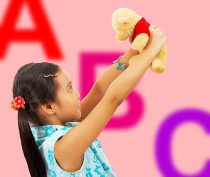 Girl Holding Her Teddy Bear Up In The Air - In Her Playroom With ABC Background