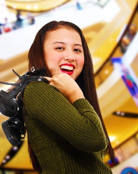 Smiling teenager in a shopping center holding her shoes over her shoulder