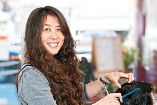 Happy hairdresser cutting hair in her salon