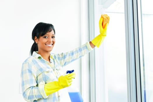 Smiling black woman cleaning windows with glass cleaner