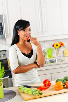 Smiling black woman tasting vegetables in modern kitchen interior