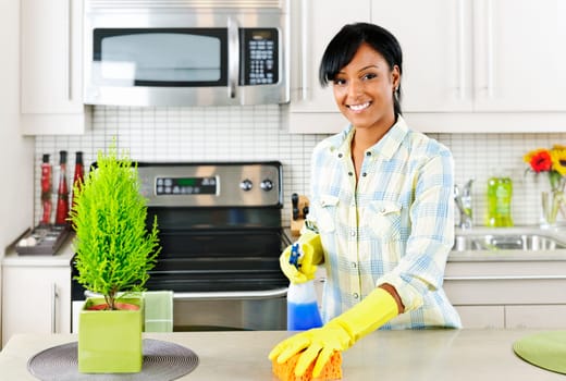 Smiling young black woman with sponge and rubber gloves cleaning kitchen