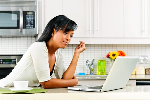 Thoughtful black woman using computer in modern kitchen interior