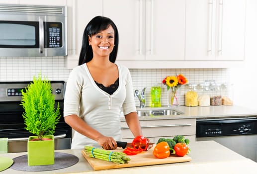 Smiling black woman cutting vegetables in modern kitchen interior
