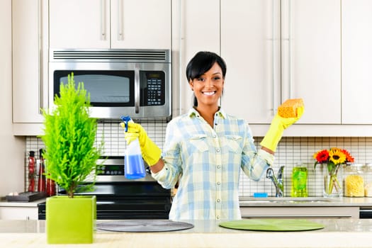 Smiling young black woman with sponge and rubber gloves cleaning kitchen